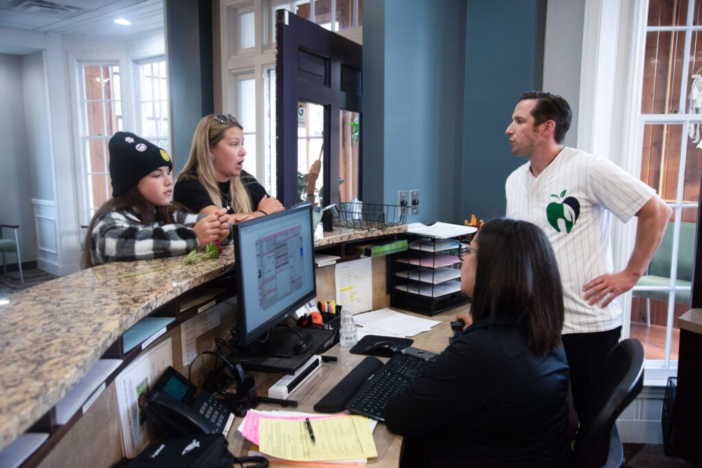 Dr. Gerald Wesley talks with a parent and her daughter at the front desk of Lifetime Orthodontics while a team member checks them in, serving families in Clinton Township and Grosse Pointe Woods