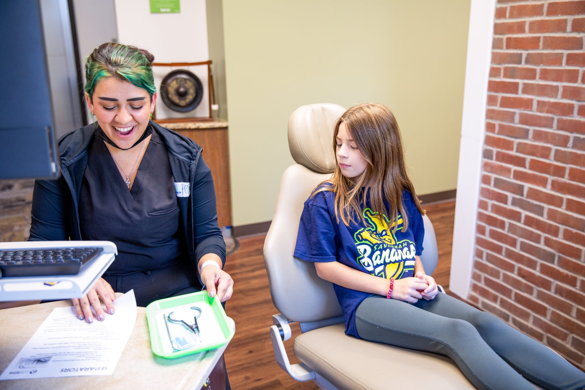 Smiling team member at Lifetime Orthodontics showing a dental model on a green tray to a young girl in a patient chair at their Clinton Township orthodontics office