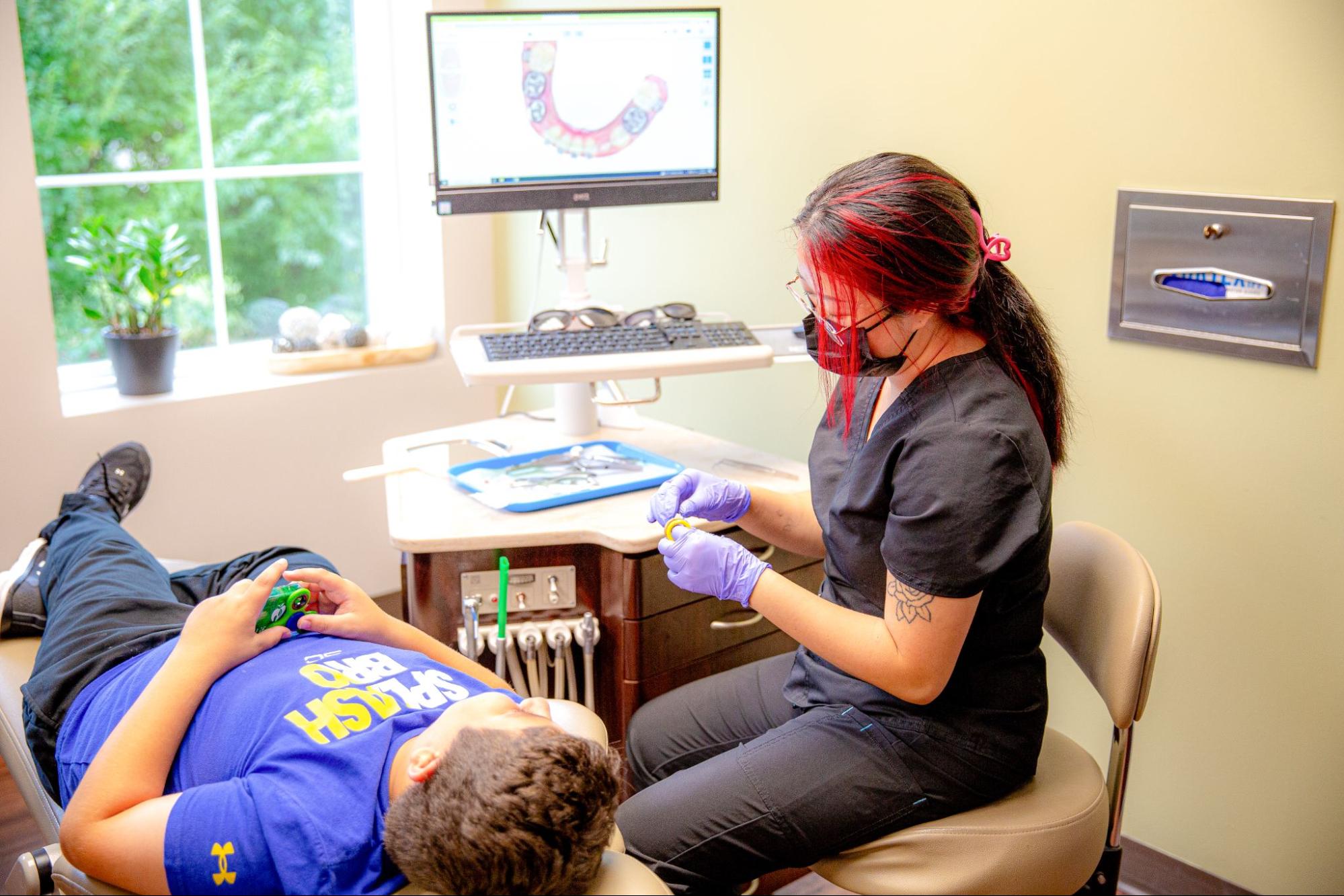 Lifetime Orthodontics team member in gloves and a mask working with a young patient in the chair, with a 3D digital tooth scan on the monitor, at the Clinton Township orthodontics office